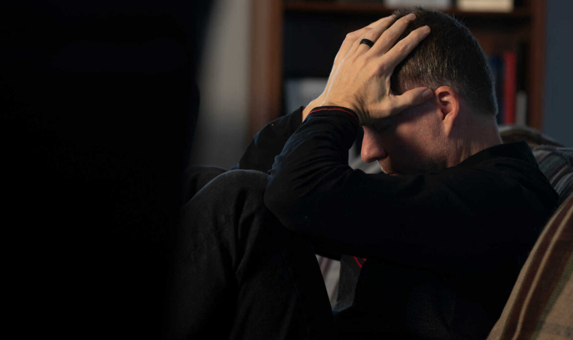 Man sitting on couch, head in hands