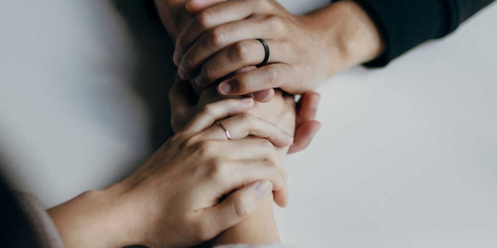 Two people holding hands across a table, symbolizing connection, care, and emotional support.