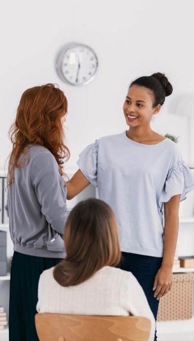 Three women engaging in a supportive group setting, with one woman offering comfort and reassurance to another